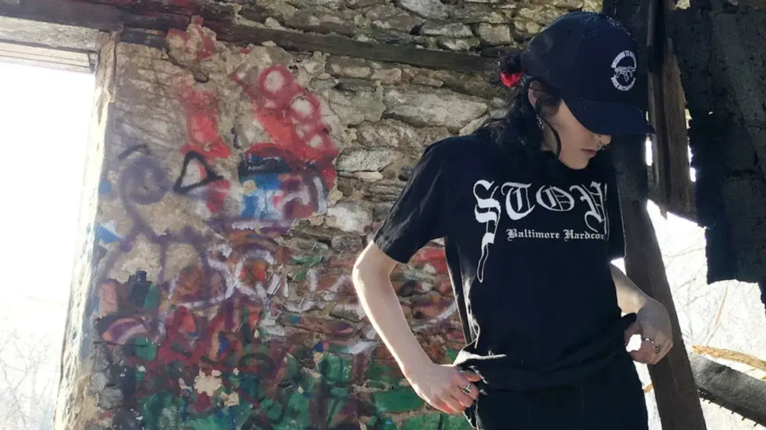 
"Model wearing a black Stout t-shirt with white text in front of a graffiti-covered wall"